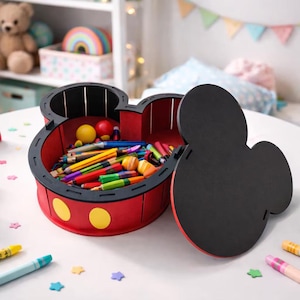 May include: A red and black Mickey Mouse-shaped storage box filled with colorful pencils and crayons. The box has yellow polka dots and a black lid. Other toys, including a wooden rainbow, are on the white table.