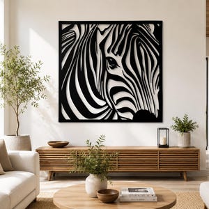 Pode incluir: Uma obra de arte de parede de zebra em preto e branco. A obra apresenta um close-up do rosto de uma zebra, com suas listras distintas. A arte é montada em uma parede branca, adicionando um toque moderno à decoração do ambiente.