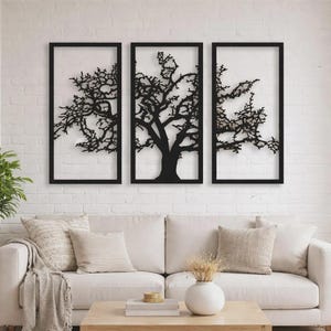 Puede incluir: Un tríptico de arte mural de metal negro con árboles. Cada pieza presenta una silueta de árbol dentro de un marco rectangular negro. La obra de arte se exhibe contra una pared de ladrillos blancos, encima de un sofá blanco con cojines.