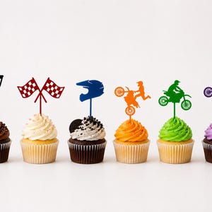 Könnte beinhalten: Sechs Cupcakes mit dekorativen Aufsätzen. Die Aufsätze umfassen eine Trophäe, karierte Flaggen, einen blauen Helm und Silhouetten von Motocross-Fahrern auf Motorrädern in Orange, Grün und Lila. Die Cupcakes haben verschiedene Glasurfarben.