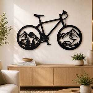 Può includere: Arte da parete a forma di bicicletta in metallo nero con ritagli di scene di montagne e foreste nelle ruote. Il pezzo decorativo è montato su una parete chiara sopra un mobile in legno, aggiungendo un tocco di arredamento ispirato alla natura.