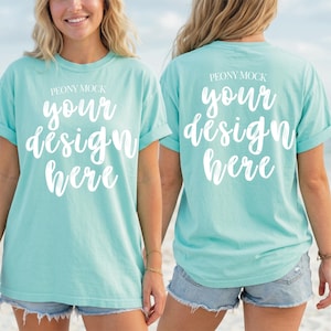 Puede incluir: Dos camisetas de color azul claro con mangas enrolladas. La parte delantera de las camisetas dice "PEONY MOCK" y "your design here" en escritura blanca. La parte trasera de las camisetas también dice "PEONY MOCK" y "your design here" en escritura blanca.
