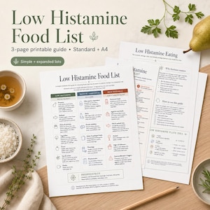 May include: A printed guide titled "Low Histamine Food List" with a 3-page layout, detailing foods to eat and avoid. The guide includes the text "Simple + expanded lists". A cup of tea and a bowl of rice are placed near the guide on a wooden surface.