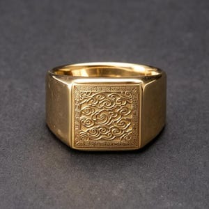 Könnte beinhalten: Ein goldfarbener Siegelring mit quadratischer Front, die ein eingraviertes Muster aus wirbelnden Wolken innerhalb einer geometrischen Umrandung zeigt. Die Ringschiene ist glatt und poliert und weist eine glänzende Oberfläche auf.