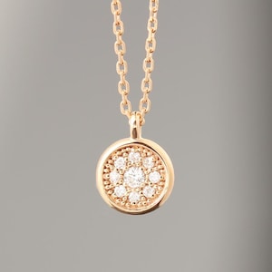 May include: A gold-colored necklace with a round pendant. The pendant is encrusted with small, sparkling stones arranged in a circular pattern around a larger central stone. The chain is delicate and also gold-colored.