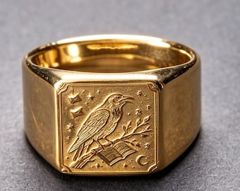 May include: A gold-toned signet ring featuring a square face with an engraved design of a raven perched on a branch above an open book. The background of the engraving includes small star shapes and a crescent moon, all rendered in a polished gold finish.