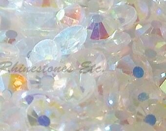 May include: A close-up image of a large quantity of iridescent white rhinestones. The rhinestones are scattered randomly and appear to be of various sizes.