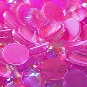 May include: Close-up of a collection of pink and magenta rhinestones. The rhinestones are a mix of round and faceted shapes, creating a sparkling effect. The image is well-lit, highlighting the different textures and colors of the gems.