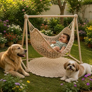 May include: A beige crocheted baby hammock suspended from a matching A-frame stand, featuring an intricate openwork pattern. A round crocheted rug sits beneath the hammock, while a golden retriever and a shih tzu lie on the grass nearby.