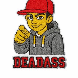 Pode incluir: Patch bordado com uma figura de desenho animado com pele amarela, usando um boné vermelho e um moletom cinza com capuz, apontando. O patch tem a palavra "DEADASS" em letras vermelhas.