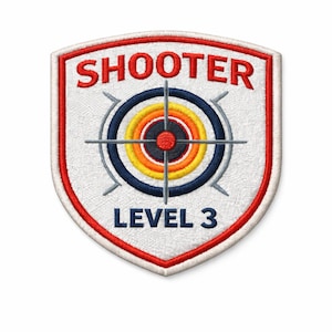 May include: Embroidered patch with a shield shape, featuring the word "SHOOTER" in red at the top and "LEVEL 3" at the bottom. The center has a target design with concentric circles in red, yellow, blue, and gray. The patch is bordered in red.
