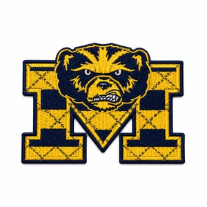 May include: An embroidered patch featuring a large letter M in navy blue and yellow. The letter has a quilted diamond pattern and is topped with a stylized, snarling bear head in matching navy blue and yellow thread with white teeth details.