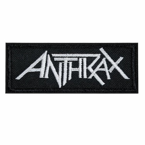 May include: A black rectangular patch with the white word "ANTHRAX" embroidered on it. The text is in a stylized, bold font, with the letters slightly overlapping. The patch has a black border.