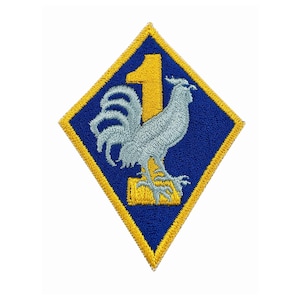 Pode incluir: Patch bordado com formato de losango azul e borda amarela. Um galo azul está representado abaixo de um número 1 amarelo. Este patch é provavelmente para um uniforme ou aplicação semelhante.