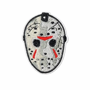 May include: Embroidered patch featuring a hockey mask design. The mask is primarily gray with black eye holes and red accents. The patch has a white border and is likely for clothing or accessories.