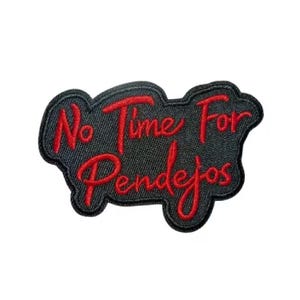 Może przedstawiać: Haftowana naszywka z napisem "No Time For Pendejos" w kolorze czerwonym na czarnym tle imitującym dżins. Naszywka ma nieregularny kształt z czerwoną obwódką, idealna do personalizacji odzieży.