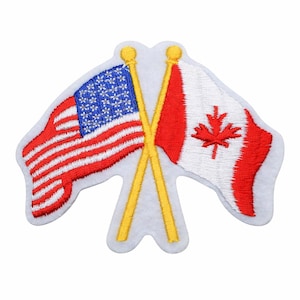 May include: Embroidered patch featuring the flags of the United States and Canada crossed. The U.S. flag has red and white stripes with a blue field of stars. The Canadian flag is red with a white maple leaf. The flags are on yellow poles.
