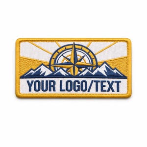 May include: Embroidered patch with a yellow border, featuring a compass rose design in blue and yellow, set against a mountain range. The patch includes the text "YOUR LOGO/TEXT" in a white banner, ideal for customisation.