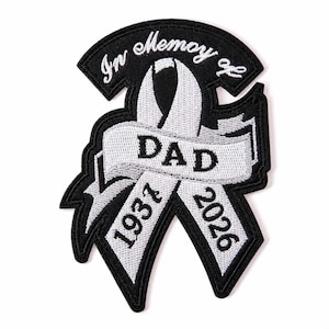 以下が含まれることがあります： 白と黒の刺繍ワッペン。リボンのデザインで、「In Memory of DAD」という文字、左側に「1937」、右側に「2026」という年号が刺繍されています。ワッペンには黒い縁取りがあり、リボンと文字は白い糸で縫い込まれています。