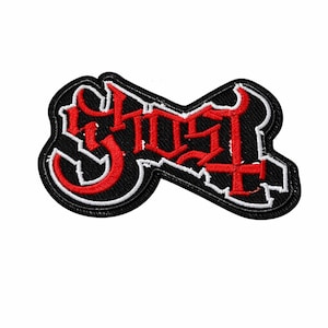 Puede incluir: Parche bordado con la palabra "Ghost" en una fuente gótica. El texto rojo tiene un contorno blanco sobre un fondo negro. El parche, con un borde negro, está diseñado para aplicarse en ropa o accesorios.