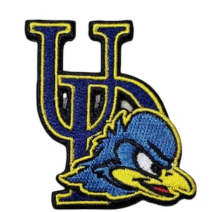 May include: Embroidered patch featuring a blue and yellow cartoon bird with a stern expression, positioned beneath a stylized blue letter "U". The patch has a black border.