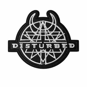 May include: A black and white embroidered patch with the word "DISTURBED" in white block letters. The patch has a circular design with geometric shapes and a curved top. The patch is likely for clothing or accessories.