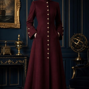 May include: A full-length, burgundy coat with a high collar and gold buttons. The coat features long sleeves with gold button details at the cuffs and pockets. The coat is floor-length and appears to be made of a wool or wool-blend fabric.