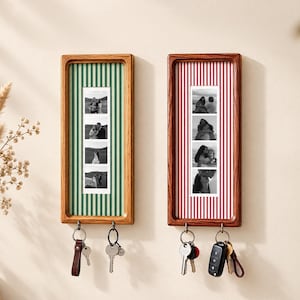May include: Two rectangular wooden wall-mounted key holders with vertical striped backings in green and red. Each frame displays a vertical strip of four black and white photographs and features two metal hooks at the bottom holding metal keys.