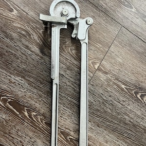 May include: A silver-colored tube bender tool with a curved head and a long handle. The tool has markings for various bending angles, including 45, 90, 135, and 180 degrees. The handle is marked "RIDGID" and "398".