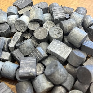 Może przedstawiać: Stos małych, szarych, cylindrycznych i prostokątnych przedmiotów. Niektóre mają teksturowane powierzchnie, podczas gdy inne są gładkie. Przedmioty są rozrzucone, o różnych kształtach i rozmiarach, tworząc teksturowany wygląd. Ogólny kolor to stonowana szarość.