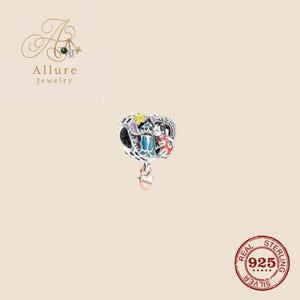 Op de afbeelding: Een zilveren bedel met een hartvormige hanger. De bedel heeft een cartoon-personageontwerp met blauwe, rode en gele accenten. De bedel is gemarkeerd met "925" en "Real Sterling Silver".