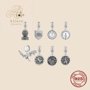 Puede incluir: Colección de colgantes de plata con varios diseños, incluyendo un trono, un escudo y colgantes circulares con detalles intrincados. Cada colgante está etiquetado "GAME" e incluye texto de la serie Juego de Tronos. Los colgantes están marcados "925 STERLING SILVER".