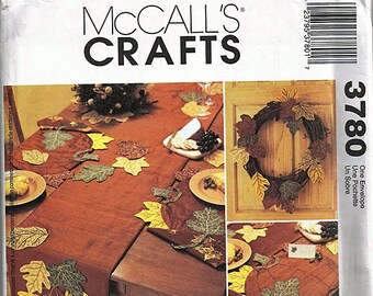May include: A sewing pattern for a fall-themed table runner, placemats, and a wreath. The pattern includes instructions for making a table runner with a leaf design, placemats with a leaf design, and a wreath with a leaf design. The pattern is from McCall's Crafts and is number 3780.