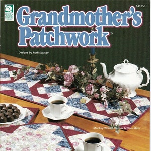May include: A book cover for a quilting pattern book titled "Grandmother's Patchwork" with a design of a table setting with a runner and placemats. The runner and placemats are made with a patchwork design of red, blue, and white fabric. The book cover also includes a teapot, cups, and a floral arrangement.