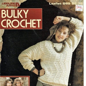 May include: A crochet pattern booklet featuring a woman wearing a white crocheted sweater and a beaded necklace. The cover also includes the text "Leisure Arts" and "Bulky Crochet".