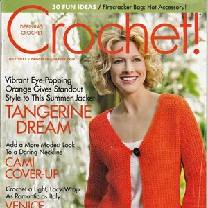 May include: The cover of a crochet magazine features a woman wearing a vibrant orange, open-front cardigan. The magazine title is "Crochet!" with text that reads "Tangerine Dream" and "Cami Cover-Up". The cover also includes the text "Venice Shawl".