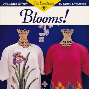 May include: A cross stitch pattern booklet titled "Blooms!" by Cathy Livingston. The cover features two white mannequins wearing cross-stitched sweaters. One sweater features a purple iris and the other features yellow tulips and blue hyacinths.