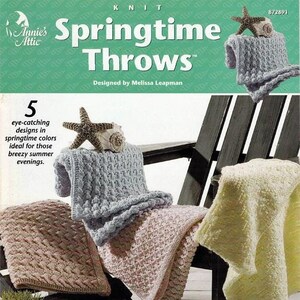May include: Five knitted throw blankets in various colors, including pink, blue, and yellow, are displayed on a wooden chair and a wooden floor. The text "Springtime Throws" is featured on the image.