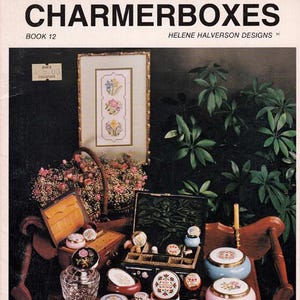 May include: A vintage magazine cover titled "CHARMERBOXES" featuring various decorative boxes, a framed floral embroidery, and a basket of flowers. The boxes are in various shapes, sizes, and colors, with floral and geometric designs.