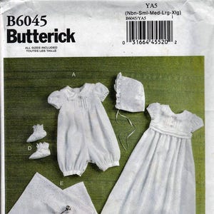 May include: A Butterick B6045 sewing pattern envelope featuring white infant clothing including a short-sleeved romper, a bonnet, a long gown, booties, and a blanket with a rattle. The text includes B6045, Butterick, YA5, and Nbn-Sml-Med-Lrg-Xlg.