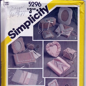 May include: Simplicity sewing pattern envelope featuring various craft projects. The projects include a heart-shaped frame, a small box, and a photo album. The envelope is yellow with the text "Simplicity" and the name "Marjorie Puckett".