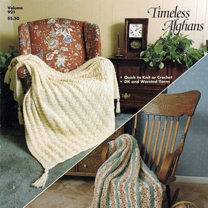 May include: Two crocheted afghans, one white and one with stripes of green, pink, and white, are draped over chairs. The text "Timeless Afghans" is at the top of the image. The text "Quick to Knit or Crochet" and "DK and Worsted Yarns" is below the image of the afghans.
