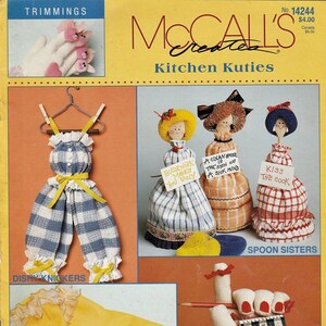 May include: A vintage McCall's pattern cover featuring kitchen-themed crafts. The image showcases various handmade items, including dish scrubbers, spoon dolls, and a pair of yellow rubber gloves with a ring and bracelet. Text includes "Kitchen Kuties" and "8 Easy Kitchen Gifts."