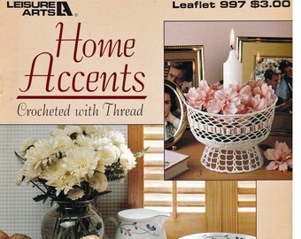 May include: A crochet pattern booklet titled "Home Accents" with a white crocheted candle holder and a white crocheted fruit bowl. The booklet is from Leisure Arts and is leaflet number 997. The booklet is $3.00.