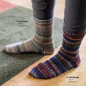 May include: Two pairs of socks, one with a brown, gray, and blue striped pattern and the other with a colorful, geometric pattern. The socks are knit in different yarns, one labeled "Comfort Sock" and the other "Berroco Sox".
