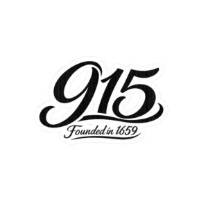 Puede incluir: Una pegatina en blanco y negro con el número "915" en una fuente cursiva. Debajo del número, el texto "Founded in 1659" está escrito en una fuente cursiva más pequeña. La pegatina está sobre un fondo blanco.