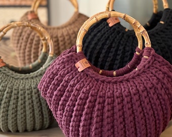 Peut inclure: Un ensemble de quatre sacs à main en forme de croissant, fabriqués en tissu tricoté épais et côtelé, déclinés en bordeaux, vert olive, noir et beige. Chaque sac possède une anse ronde en bambou et une petite étiquette en cuir.