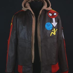 Pu&ograve; includere: Una giacca in pelle marrone scuro con uno strato interno con cappuccio color marrone chiaro, polsini e orlo a coste rossi e strisce laterali rosse. La parte anteriore &egrave; decorata con toppe ricamate tra cui una maschera da ragno rossa e una freccia bianca.