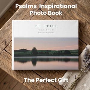 May include: A photo book titled "Psalms Inspirational Photo Book" with the text "Be Still and Know." The book features a landscape image of a lake and trees. The words "The Perfect Gift" are at the bottom. The book is on a wooden surface.