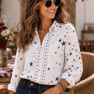 May include: A white long-sleeved button-down shirt featuring a scattered pattern of red and blue stars. The shirt includes a vertical decorative stripe along the button placket composed of smaller red and blue stars, a classic collar, and cuffed sleeves.